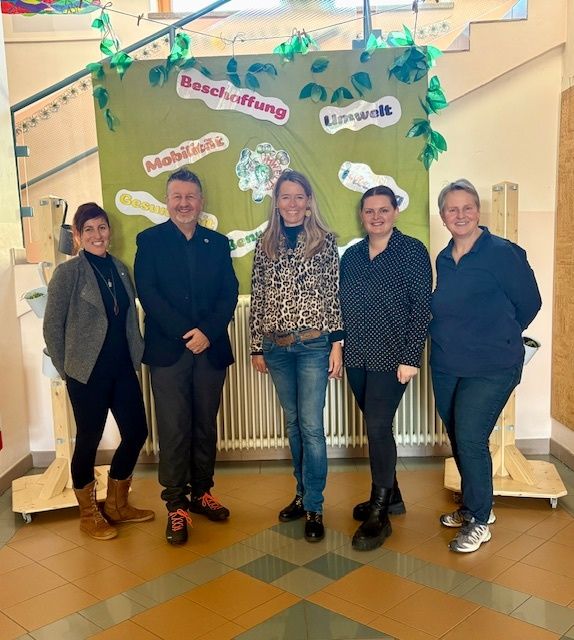 Fünf Personen stehen gemeinsam vor einem grünen Banner mit den Aufschriften 'Mobilitaet' und 'Beschaffung'. Sie alle lächeln für die Kamera.