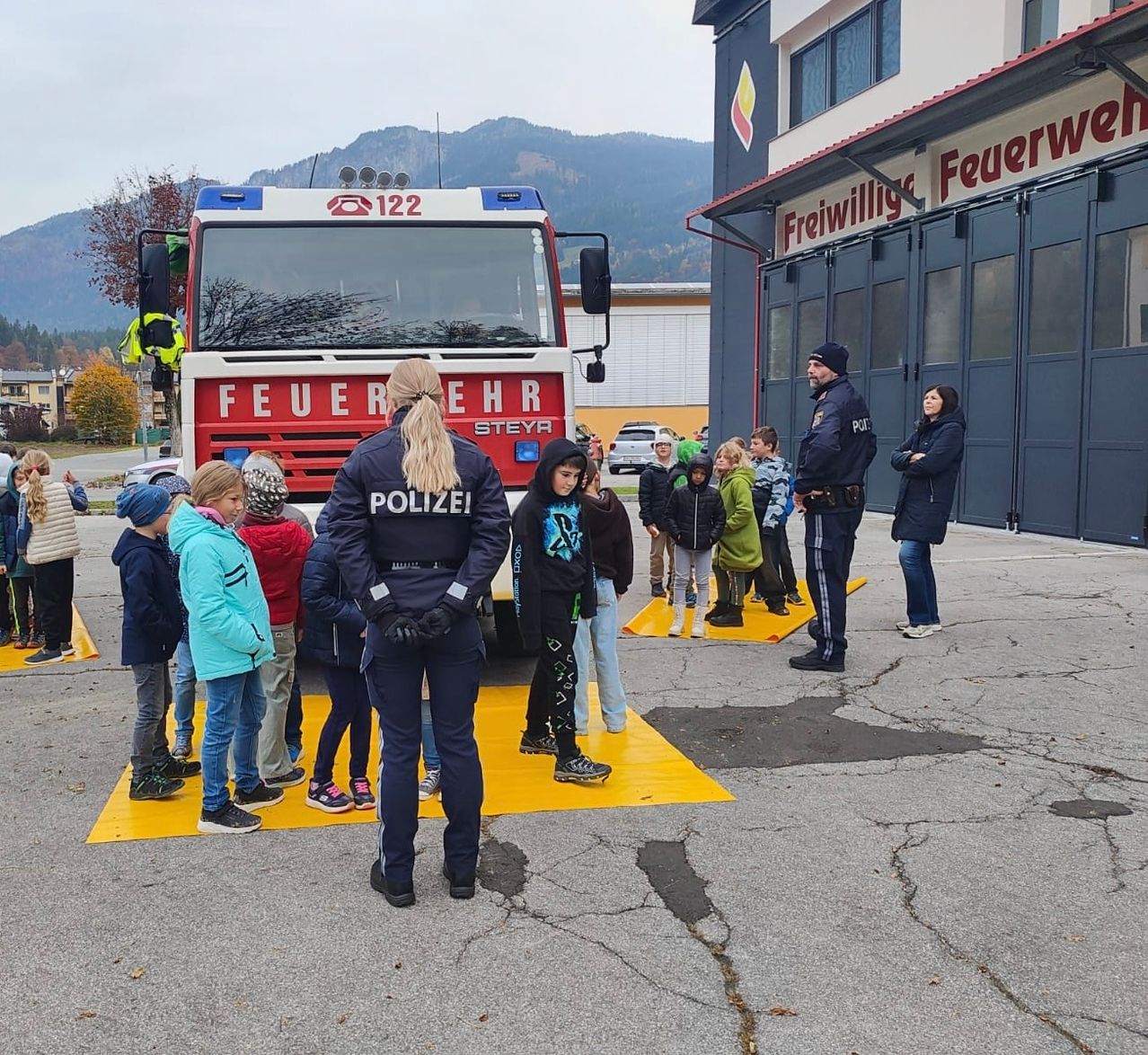 Eine Gruppe von Kindern und Erwachsenen steht vor einem Feuerwehrauto. Sie sind draußen vor einer Feuerwache.