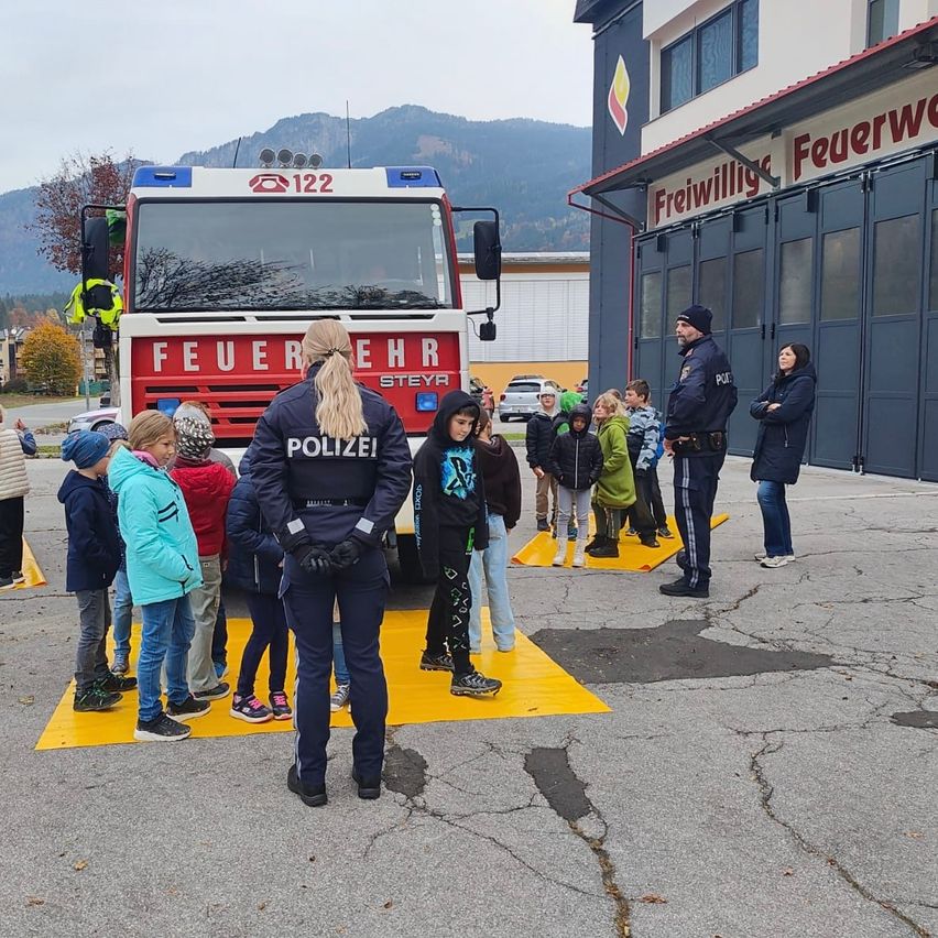 Eine Gruppe von Kindern und Erwachsenen steht vor einem Feuerwehrauto. Sie sind draußen vor einer Feuerwache.