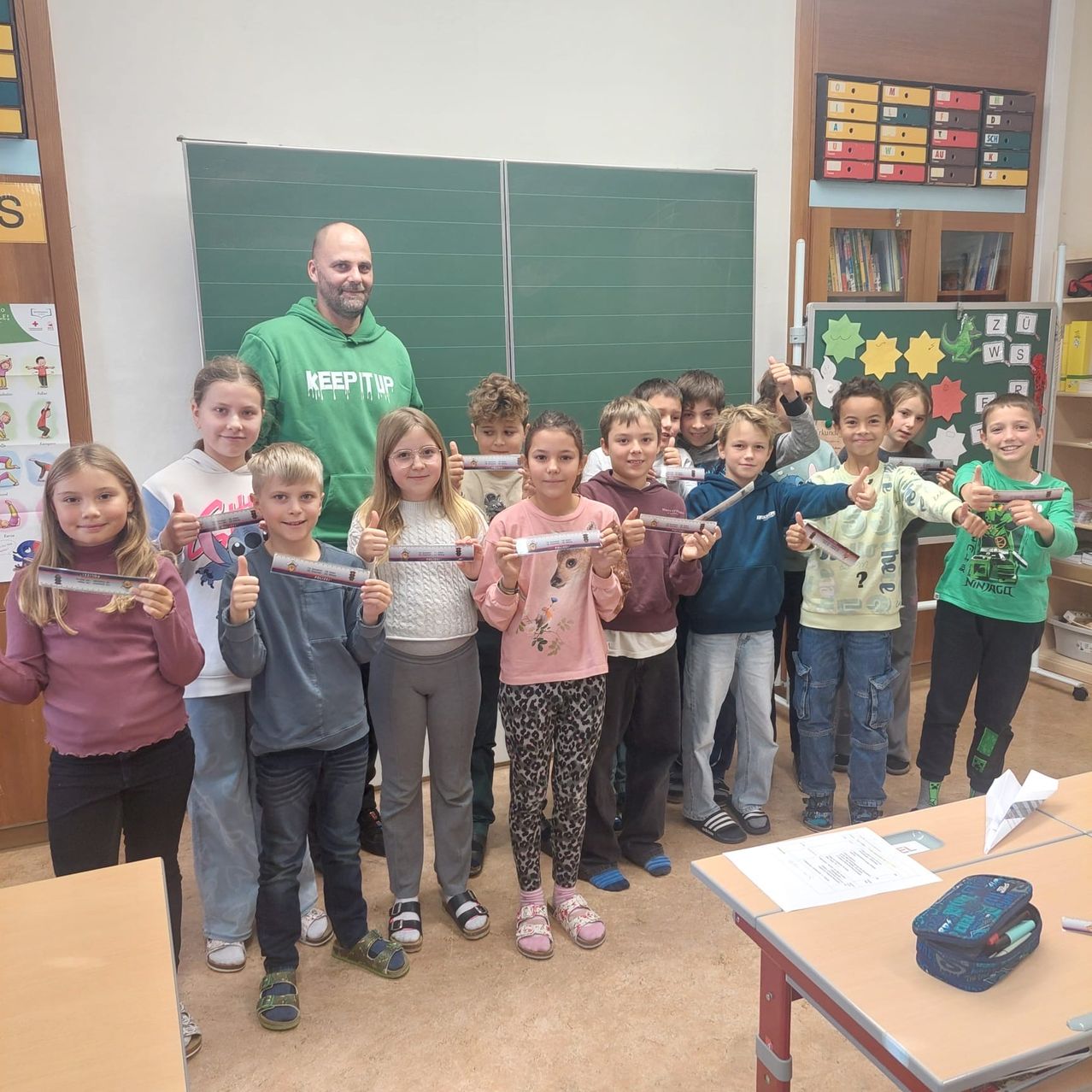 Eine Gruppe von Kindern und ein Mann posieren für ein Foto im Klassenzimmer und halten gerolltes Papier.