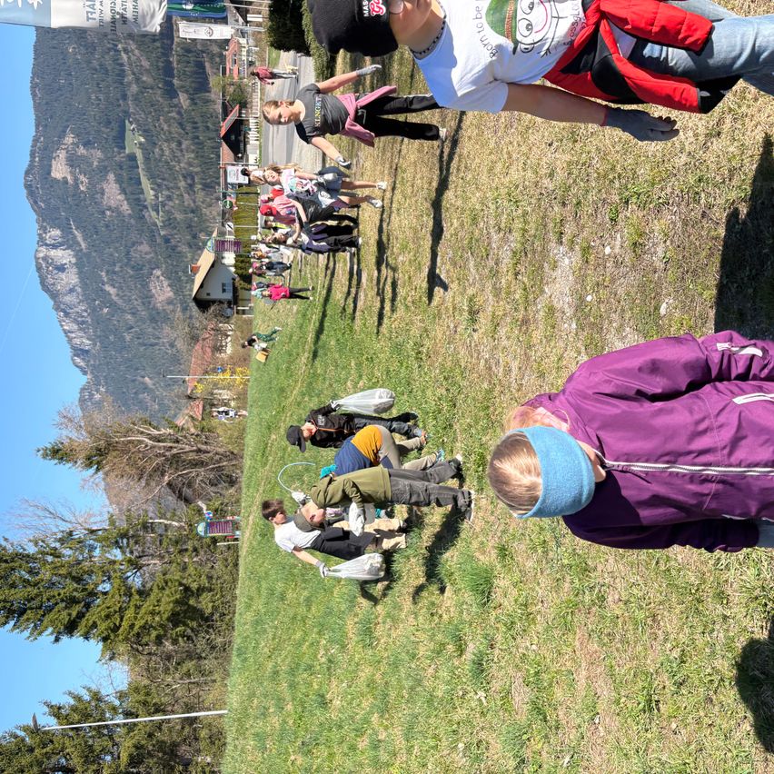 Eine Gruppe von Menschen befindet sich auf einem Grasfeld mit Bergen im Hintergrund. Sie machen wahrscheinlich Aktivitäten.