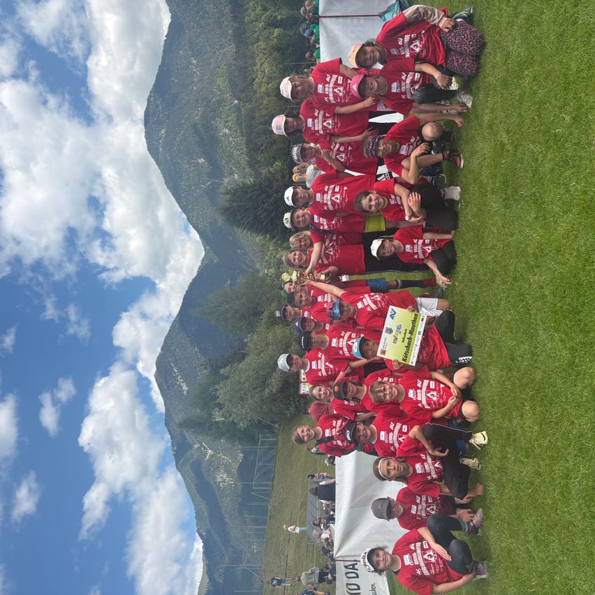 Eine Gruppe von Menschen in roten T-Shirts posiert für ein Foto auf einem Feld mit einem Berg im Hintergrund.