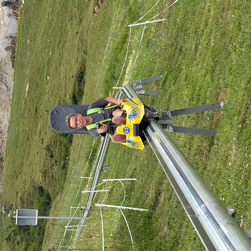 Ein junger Junge mit Brille fährt eine gelbe Rutsche auf einer Metallkonstruktion über einem Grasfeld.