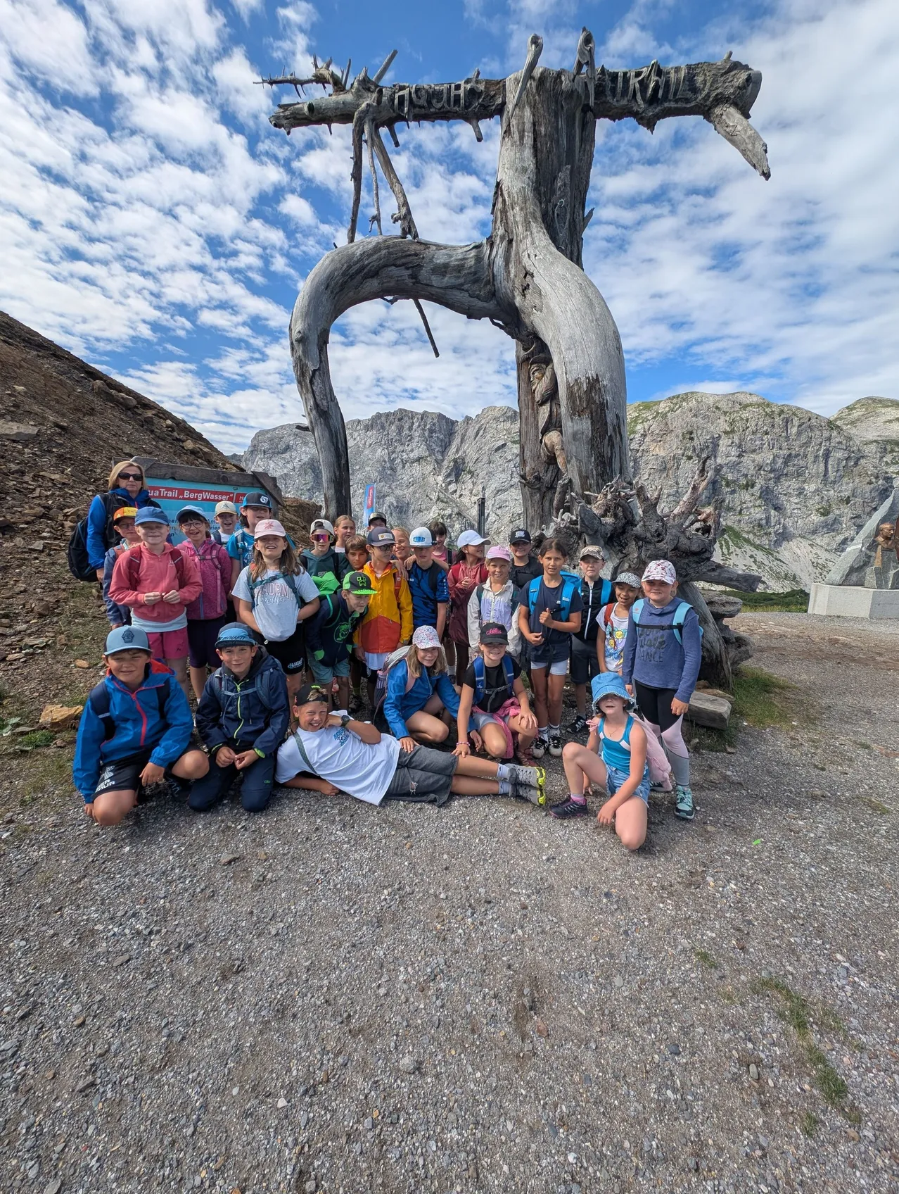 Eine Gruppe von Kindern und Erwachsenen posiert für ein Foto vor einem großen Baumstamm in einem Berggebiet.