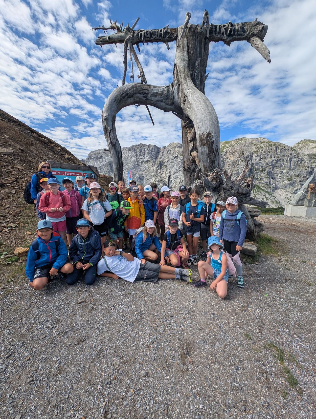 Eine Gruppe von Kindern und Erwachsenen posiert für ein Foto vor einem großen Baumstamm in einem Berggebiet.