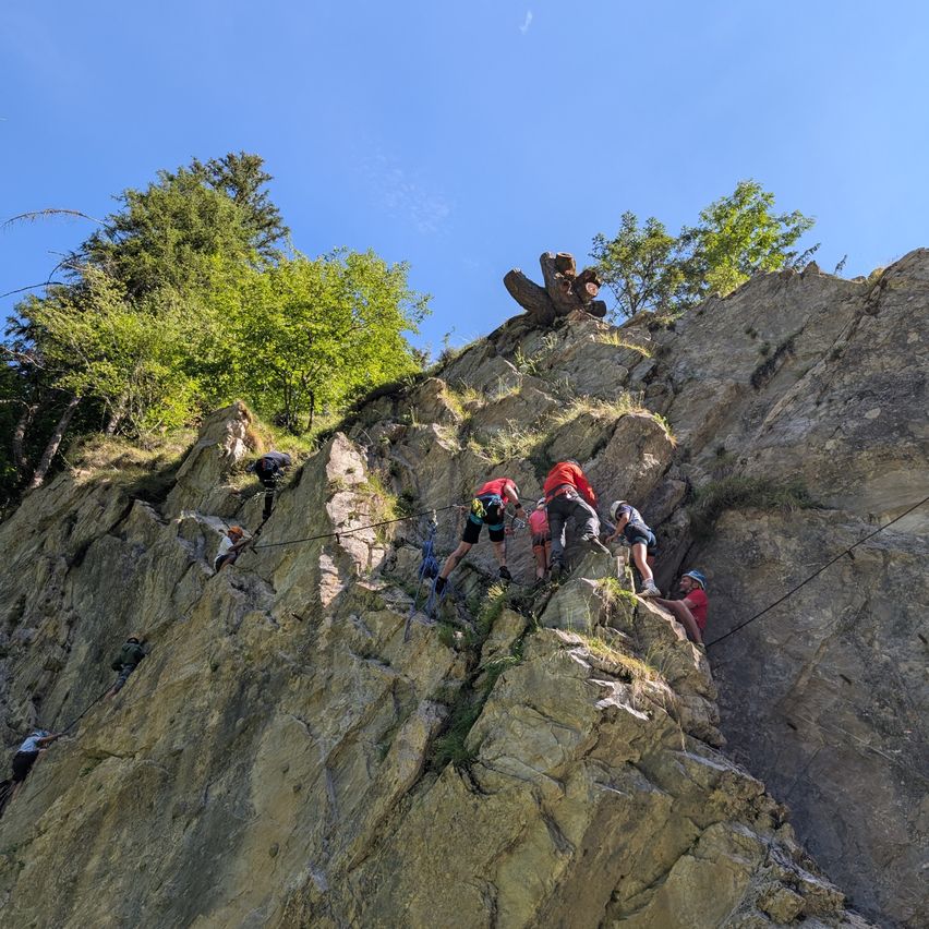 Eine Gruppe von Kletterern erklimmt einen steilen felsigen Fels unter blauem Himmel und benutzt Seile zur Sicherheit.