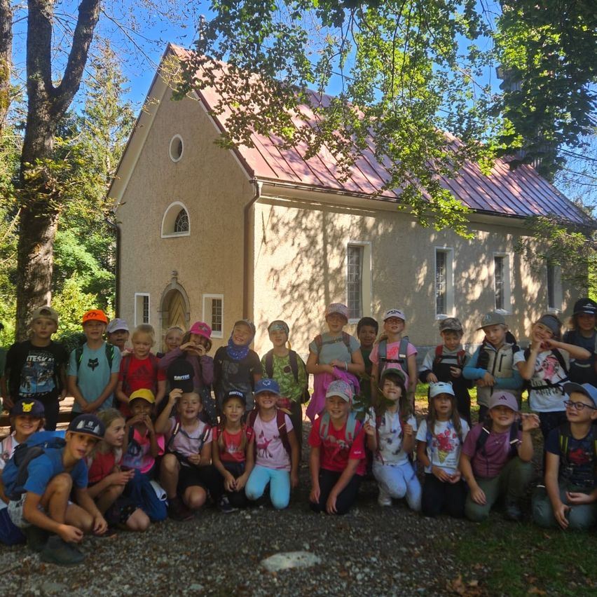 Eine Gruppe von Kindern in Mützen und Rucksäcken posiert für ein Foto vor einer kleinen Kapelle.