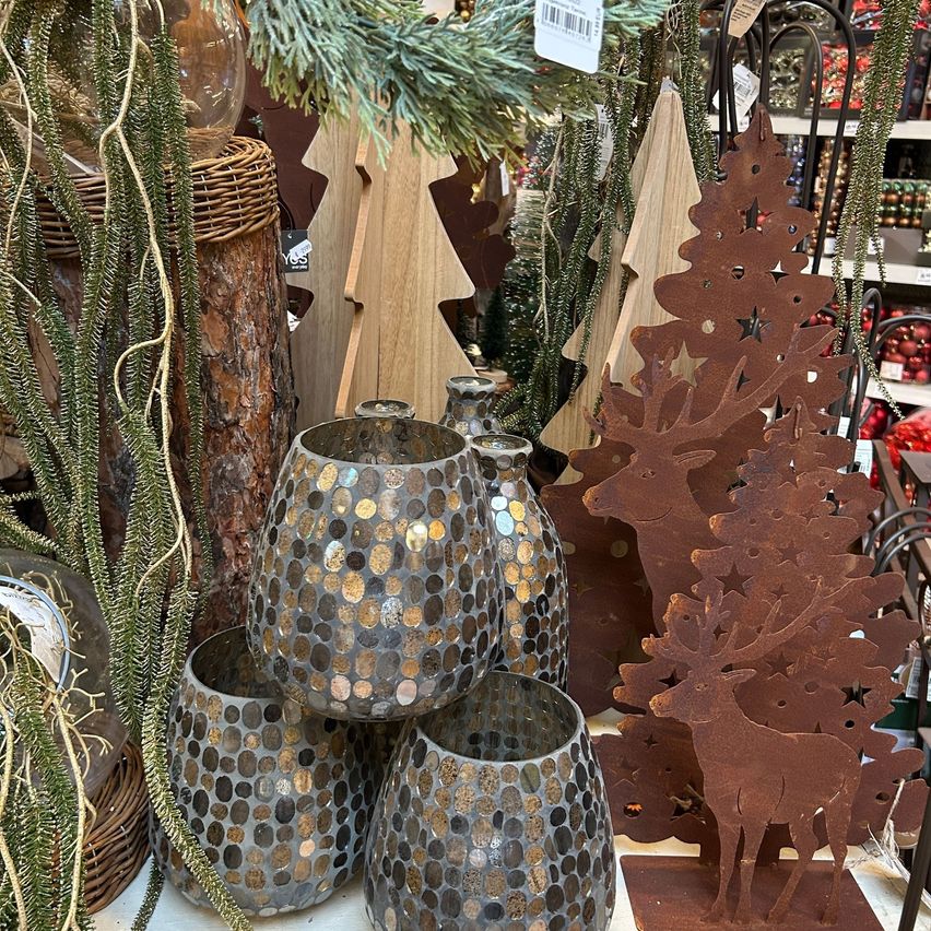 Eine Ausstellung von Dekorationsartikeln in einem Geschäft mit einem rustikalen Holzbaum, einer braunen Rentierstatue und vier gesprenkelten Glasvasen auf einer Holzoberfläche.