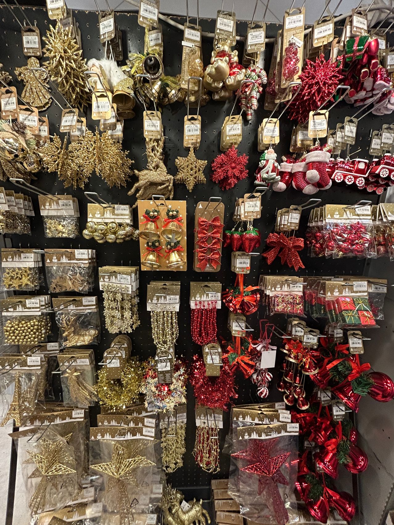 A variety of Christmas decorations are displayed on a wall, including gold and red ornaments, gift boxes, and Santa Claus figures. The decorations are hanging on hooks and organized in clear plastic bags.
