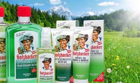 Ein Bild zeigt verschiedene Flaschen und Tuben von Franzbranntwein Produkten in einem grünen und weißen Farbschema, vor dem Hintergrund einer grünen, üppigen Wiese mit Bergen und Sonnenschein.