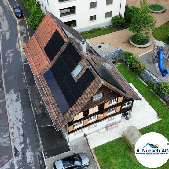 Eine Draufsicht auf ein Haus mit Solarmodulen auf dem Dach, einem geparkten Auto und einem Gebäude mit Balkonen.