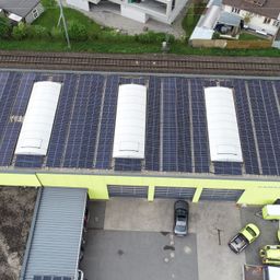 Eine Draufsicht auf ein Gebäude mit Solarpanels auf dem Dach und mehreren Autos, die auf dem Parkplatz geparkt sind.