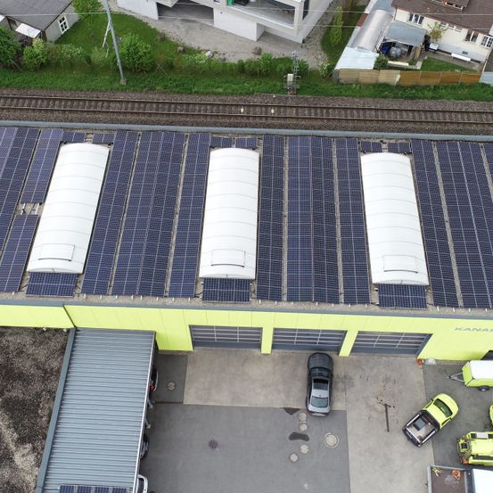 Eine Draufsicht auf ein Gebäude mit Solarpanels auf dem Dach und mehreren Autos, die auf dem Parkplatz geparkt sind.