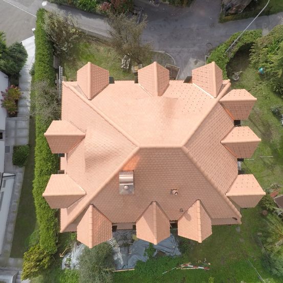 Eine Luftaufnahme eines Hauses mit einem einzigartigen achteckigen Dach aus Terrakotta-Fliesen, umgeben von Grünflächen und einer Auffahrt.