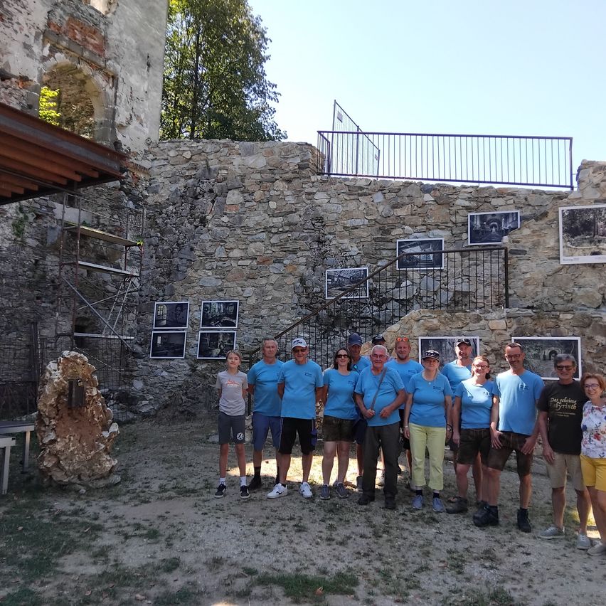 A group of people in blue shirts pose for a photo in front of a stone wall with pictures and a staircase.
