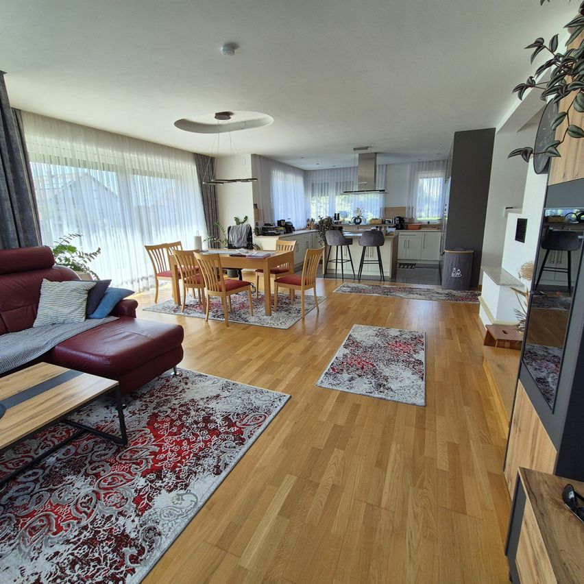 Ein modernes offenes Wohnraumdesign mit Holzböden, einem roten Sofa, einem Esstisch mit Stühlen und einem Küchenbereich mit Herd und Kühlschrank.