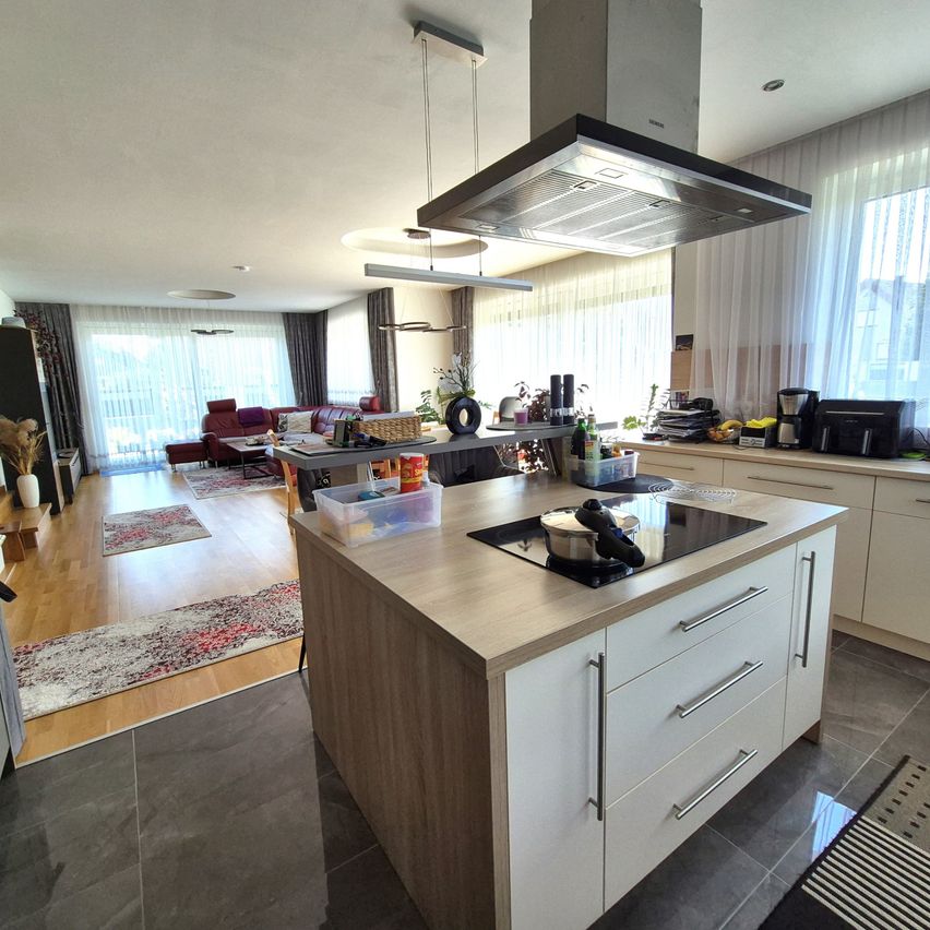 Ein offener Wohn- und Küchenbereich mit schwarzem Herd, modernen Schränken und einem Essbereich mit Couch. Die Küche hat eine weiße Decke und einen gefliesten Boden.