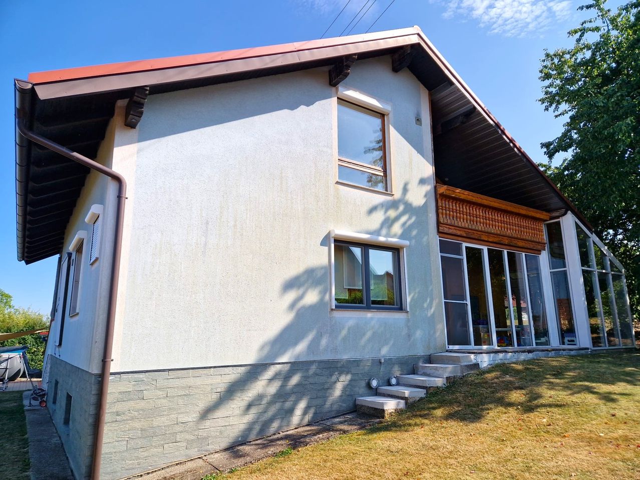 A modern house with a red roof and white walls, featuring glass windows and doors, and a small balcony with wooden railings.