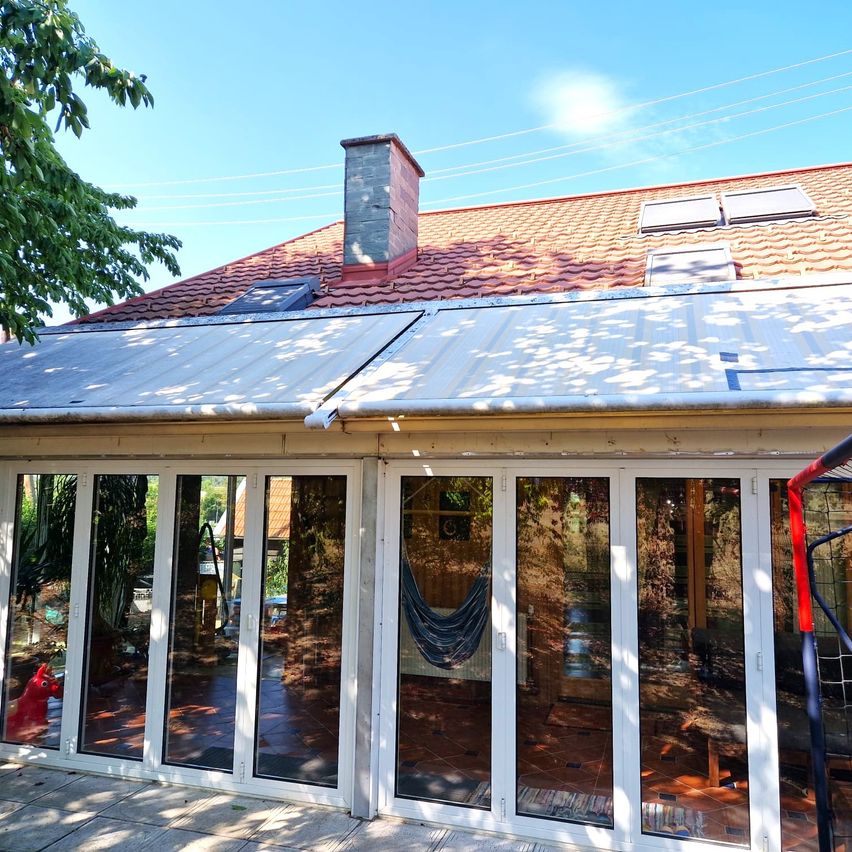 A modern house with a red tiled roof and solar panels, featuring a glass patio with a hammock hanging inside.
