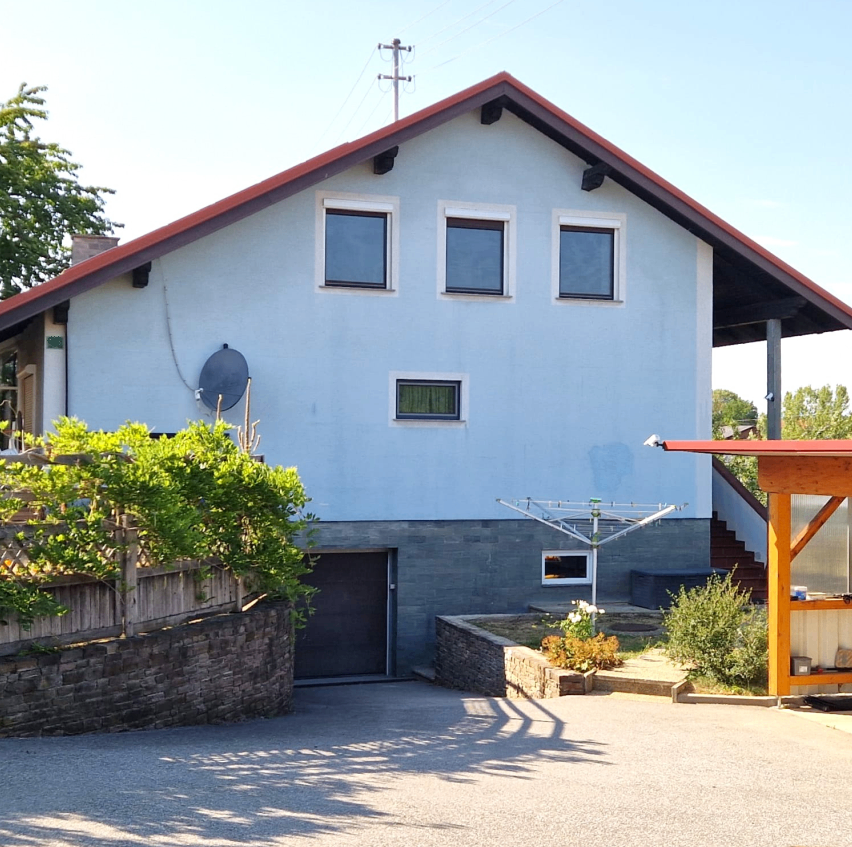 A light blue house with a red roof and a satellite dish on the wall. A garage door is on the left side of the house.