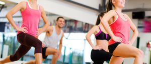 A group of people are exercising in a gym. The woman on the right is running, while the woman on the left is smiling. The man in the middle is squatting.