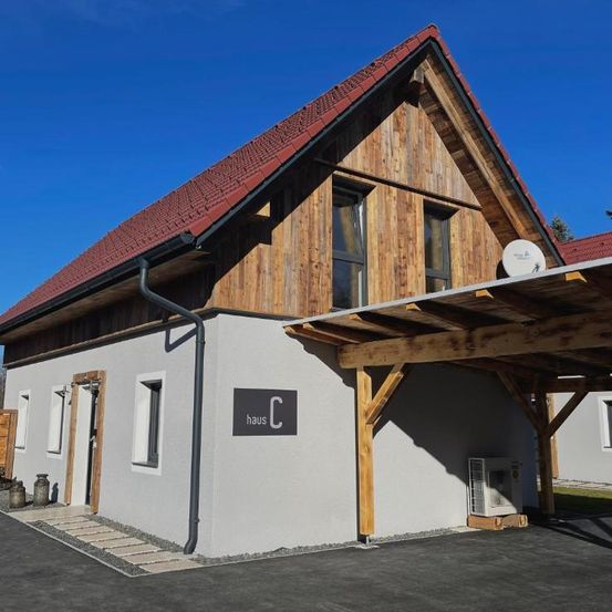 Ein modernes Haus mit rotem Dach und hölzerne Außenseite. Das Haus hat zwei Fenster und eine überdachte Carport. Das Etikett 'haus C' befindet sich an der Wand.