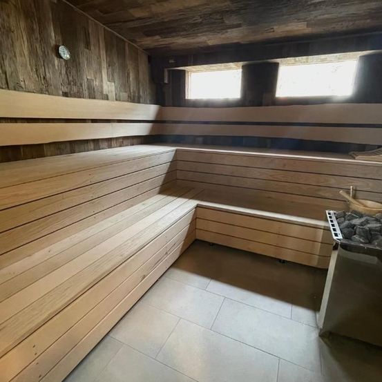 Ein Holzsaunaraum mit Holzbänken und gefliesten Böden. An der Wand ist eine kleine Uhr montiert.