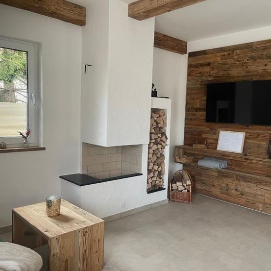 Ein modernes Wohnzimmer mit Kamin, einem an der Wand montierten Flachbildfernseher und einem Holztisch mit einem Kerzenhalter.