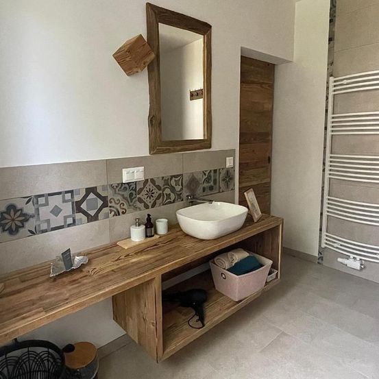 Ein Badezimmer mit einem Holzwaschbecken, einem Spiegel und einem Handtuchhalter. Die Wände haben gemusterte Fliesen und eine Holztür.