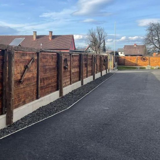 Eine Nachbarschaftsstraße mit Holzzäunen und Asphaltauffahrt, Häusern mit Schornsteinen und Solarpanels auf den Dächern.