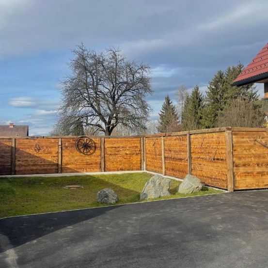 Ein Hinterhof mit Holzzaun, Rad, Felsen und einem Haus mit rotem Dach. Der Rasen ist grasig mit einem Baum im Hintergrund.