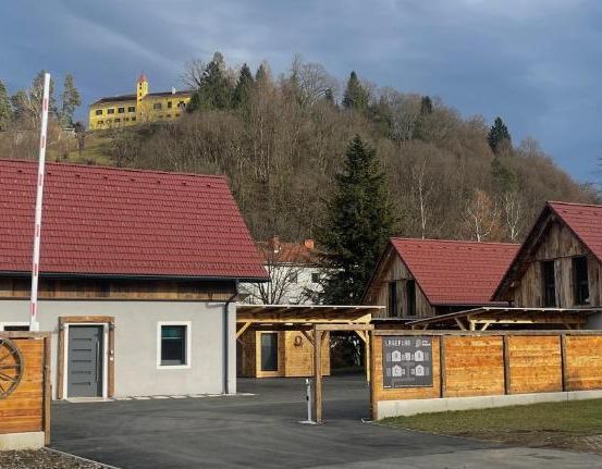 Eine kleine ländliche Gemeinde mit einem rotgedeckten Haus und einem Holzzaun. Ein gelbes Gebäude ist in der Ferne sichtbar.