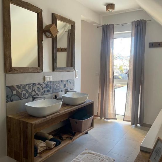 Ein Badezimmer mit zwei Waschbecken auf einer Holzkonsole, Holzspiegeln und einem Fenster mit Vorhängen.