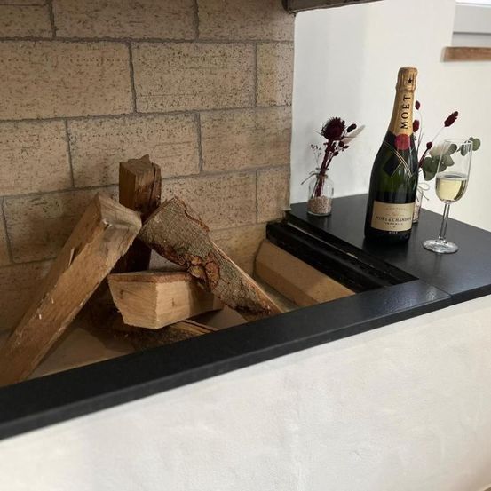 Ein Kamin mit einer Flasche Moet, zwei Weingläsern und einem Holzstapel. Im Hintergrund steht eine kleine Vase mit Blumen.