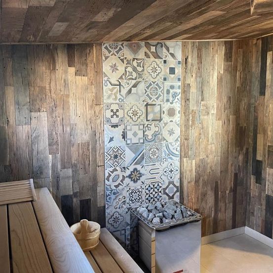 Ein kleiner Holzsaunaraum mit Holzbänken, einem Steinheizer und einer mit Fliesen verzierten Holzwand.