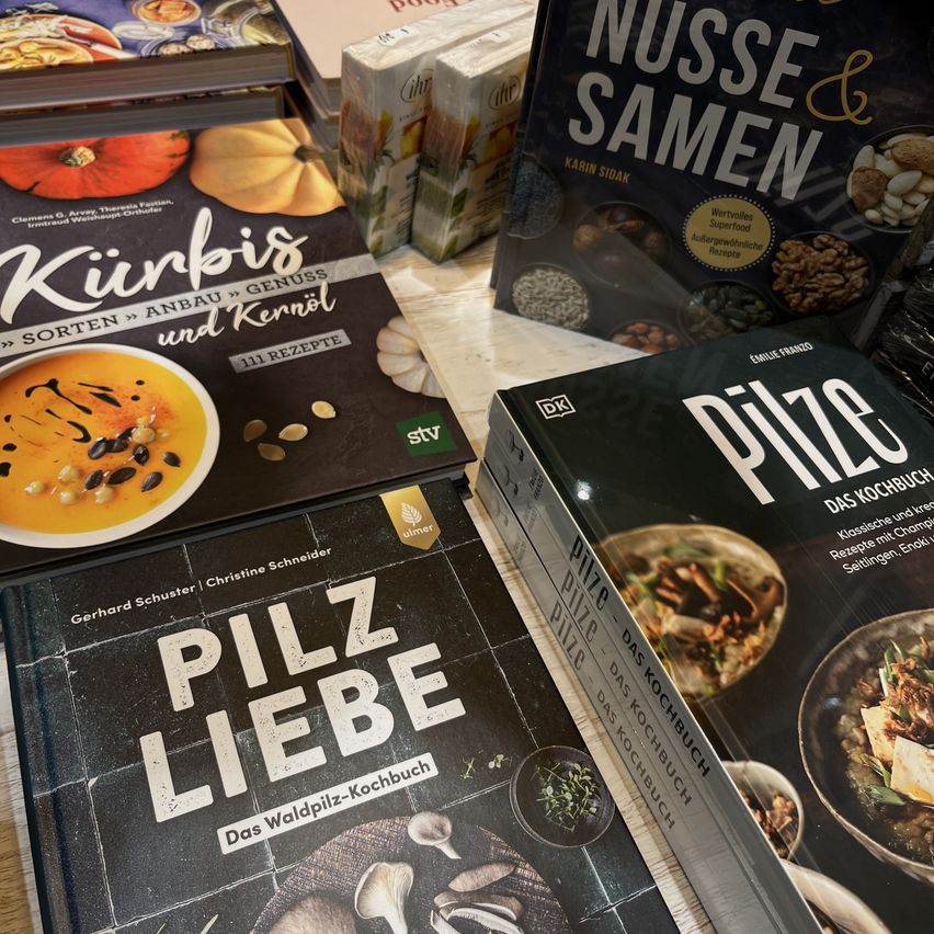 Mehrere Kochbücher sind zusammengestapelt, darunter 'Kirbis Sorten Anbau und Kernol', 'Pilze Das Kochbuch' und 'Nusse und Samen'. Jedes Buch zeigt auf seinem Cover farbenfrohe, appetitliche Gerichte.