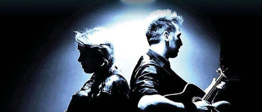 Ein Schwarz-Weiß-Bild von zwei Personen, die mit Gitarren sitzen. Eine Person hält eine Gitarre und eine andere spielt sie. Der Text auf dem Bild lautet 'WHY CRY JOHNNY'.