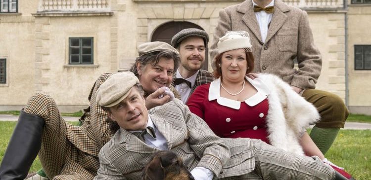 Eine Gruppe von Menschen in Vintage-Kleidung posiert vor einem historischen Gebäude, lächelt und posiert mit einem Hund.