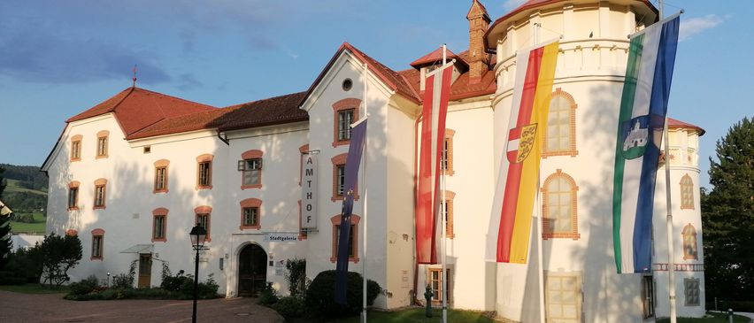 Ein weißes Gebäude mit rotem Dach und mehreren Fahnen, einschließlich der EU-Flagge, vor einem Rasen.