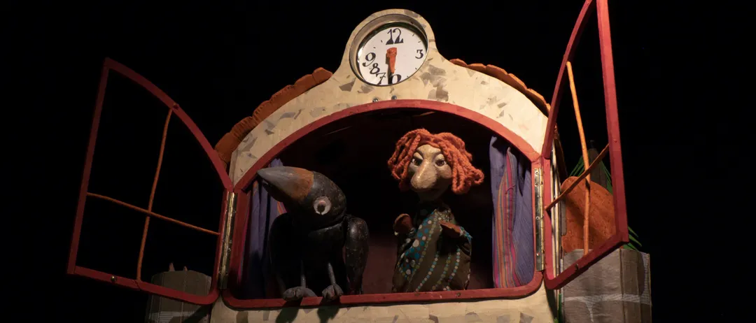 Eine Puppe mit roten Haaren und ein schwarzer Vogel in einem Uhrenturm. Die Uhr zeigt 10:10 Uhr an.