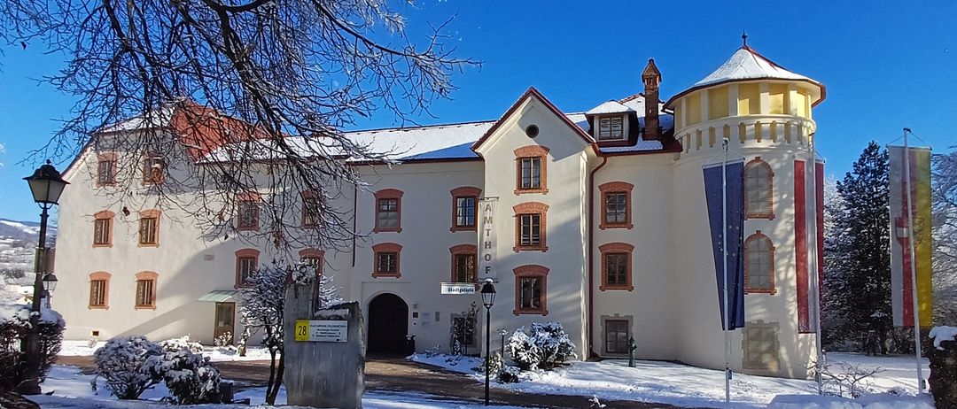 Eine schneebedeckte Außenansicht eines großen Gebäudes mit mehreren Fenstern und einem Turm, umgeben von schneebedeckten Pflanzen und Bäumen, mit Fahnen auf Stangen.