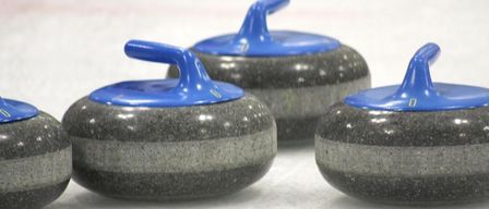 Three curling stones with blue handles are on a white surface. They are gray and black, with a small indentation on the top.