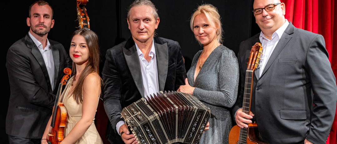 Eine Gruppe von Musikern posiert mit ihren Instrumenten. Ein Mann hält ein Akkordeon, eine Frau neben ihm eine Gitarre. Hinter ihnen spielt eine Frau Geige und ein Mann Cello.