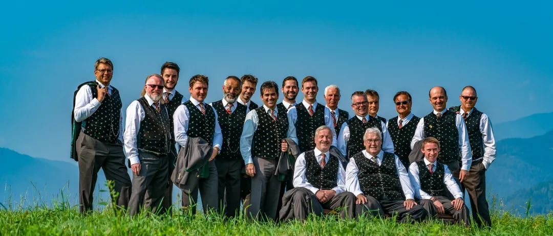 Eine Gruppe von Männern in traditioneller Kleidung posiert für ein Foto auf einer Wiese mit Bergen im Hintergrund.
