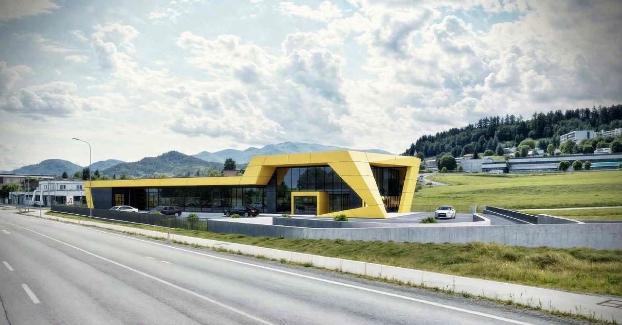 Ein modernes gelbes Gebäude mit Glaswänden steht am Straßenrand, mit mehreren Autos vor der Tür. Die Landschaft zeigt Berge und grüne Felder im Hintergrund.