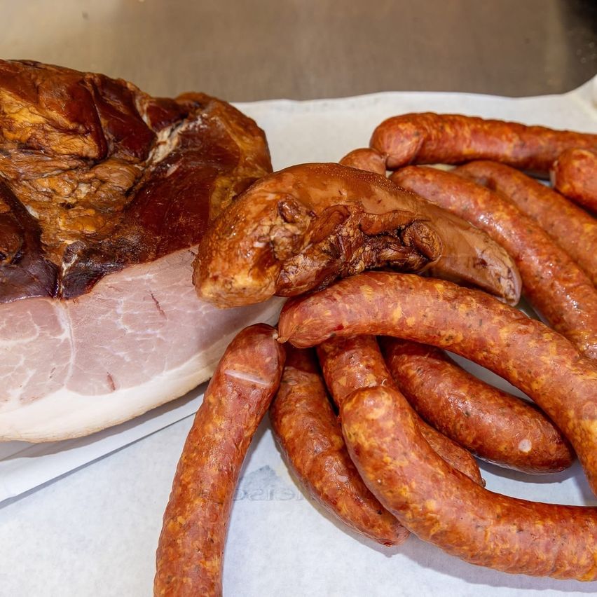 A close-up of various cured meats. Ham on the left, several sausages on the right, all on a white surface.