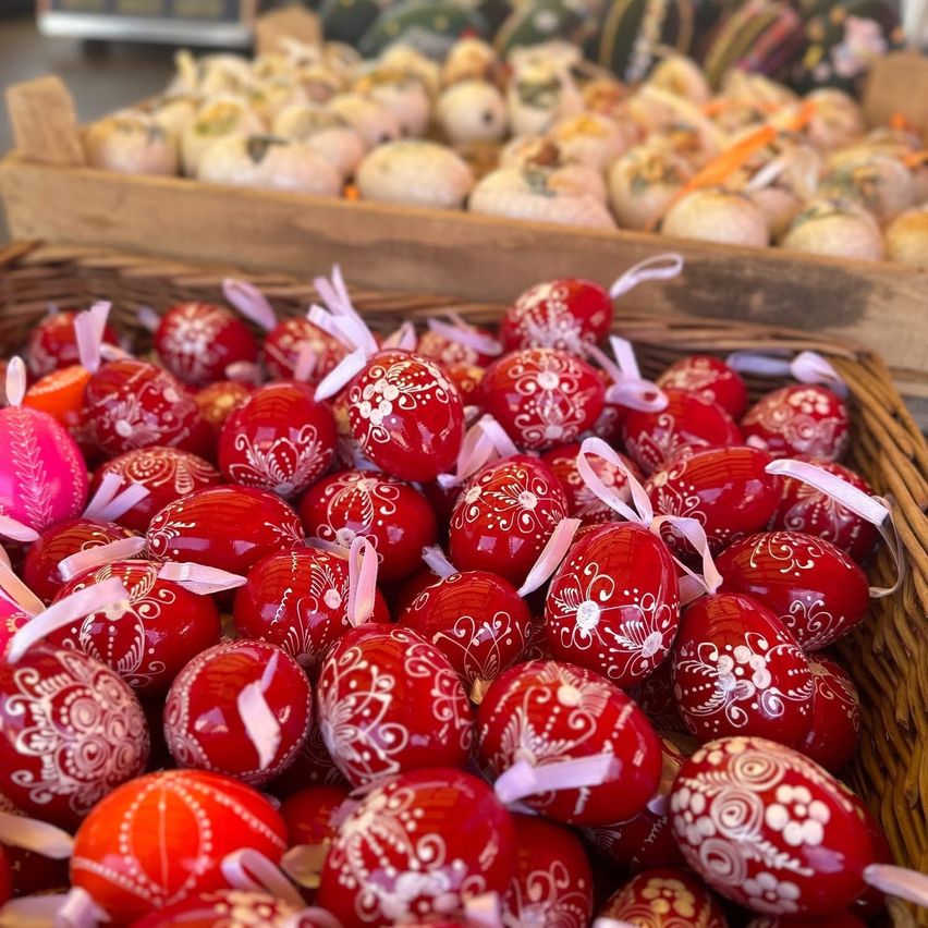 A basket filled with vibrant red eggs with intricate white designs on them, placed in front of a wooden box containing various pastries.
