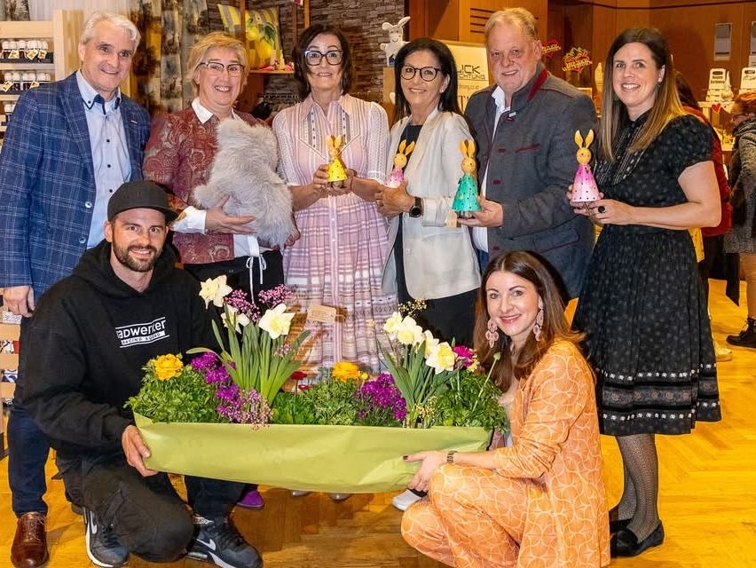 Eine Gruppe von Männern und Frauen posiert für ein Foto mit Hasendekorationen und Blumen, wahrscheinlich bei einer Veranstaltung.