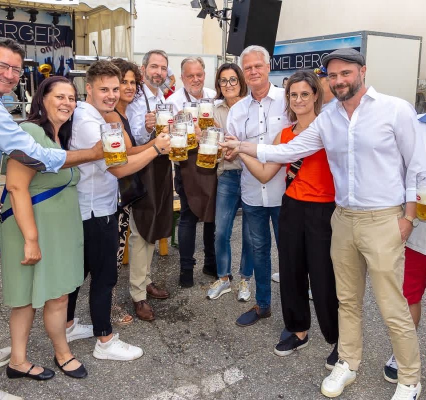 A group of people stands together holding beer mugs in an outdoor setting, likely at a festival.