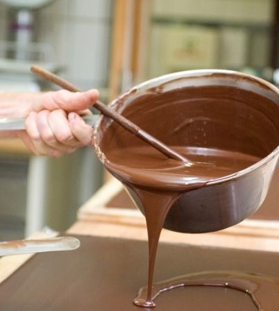 Eine Person gießt Schokolade aus einer Schüssel auf einen Holztisch.